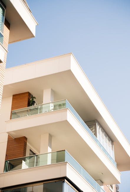 Two professional window cleaners wearing safety harnesses and helmets are performing surface cleaning and sanitisation of the large glass windows on the exterior of a modern, multi-storey building in